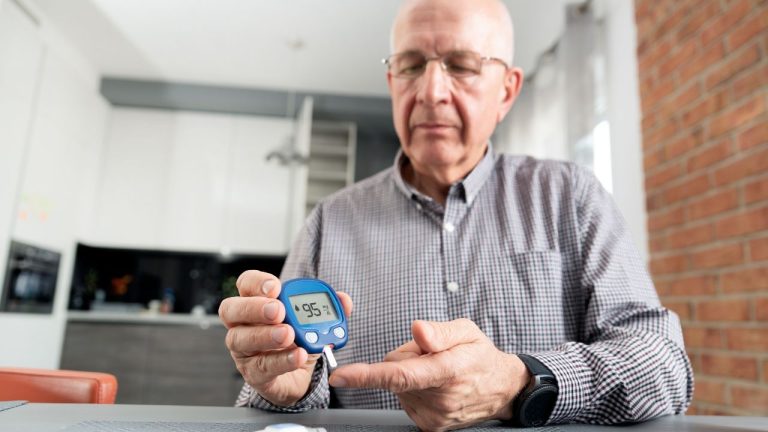 Starszy mężczyzna używa glukometru do sprawdzenia poziomu cukru we krwi w domowym otoczeniu.