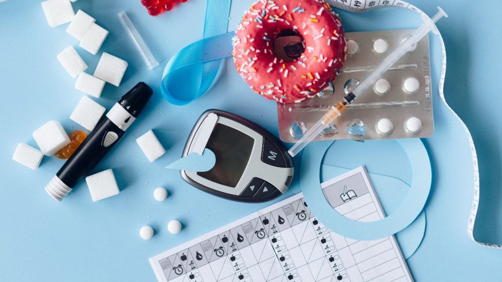 Kompozycja przedstawiająca przedmioty związane z zarządzaniem cukrzycą, w tym glukometr, insulinę, środki iniekcyjne, słodycze, tabletki i diagram samokontroli cukru we krwi, na tle w kolorze błękitnym.