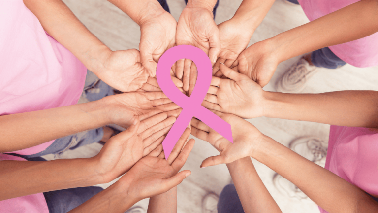 Zdjęcie pokazuje wiele rąk trzymających różową wstążkę, symbolizującą wsparcie i świadomość walki z rakiem piersi.