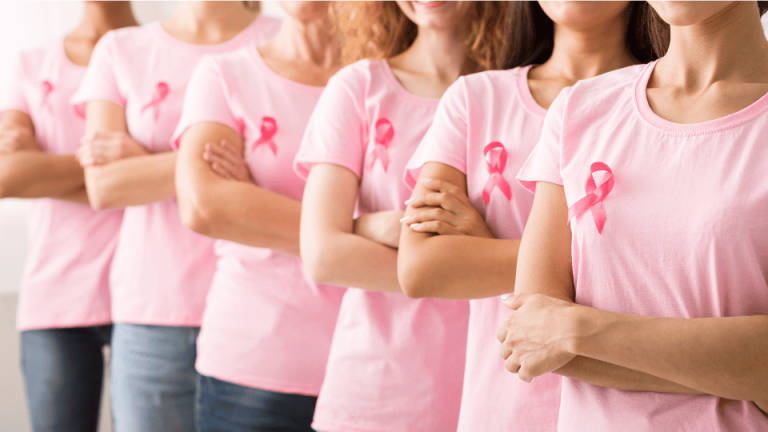 Grupa kobiet ubranych w różowe koszulki z różowymi wstążkami, stojących ramię w ramię, symbolizujących solidarność i wsparcie w walce z rakiem piersi.