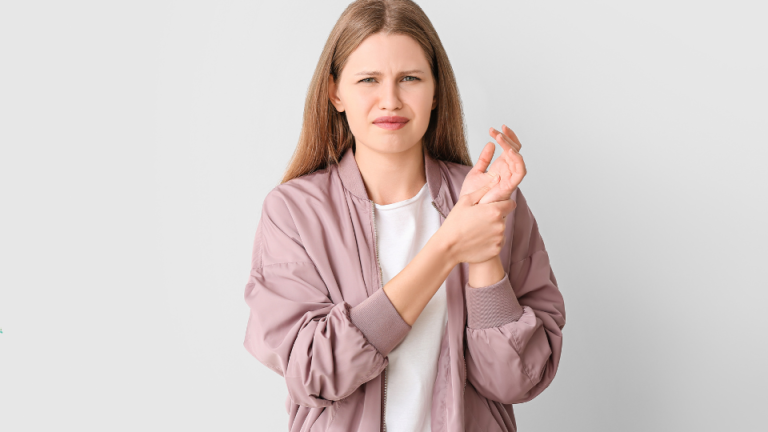 Młoda kobieta z bolesnym wyrazem twarzy trzyma się za nadgarstek